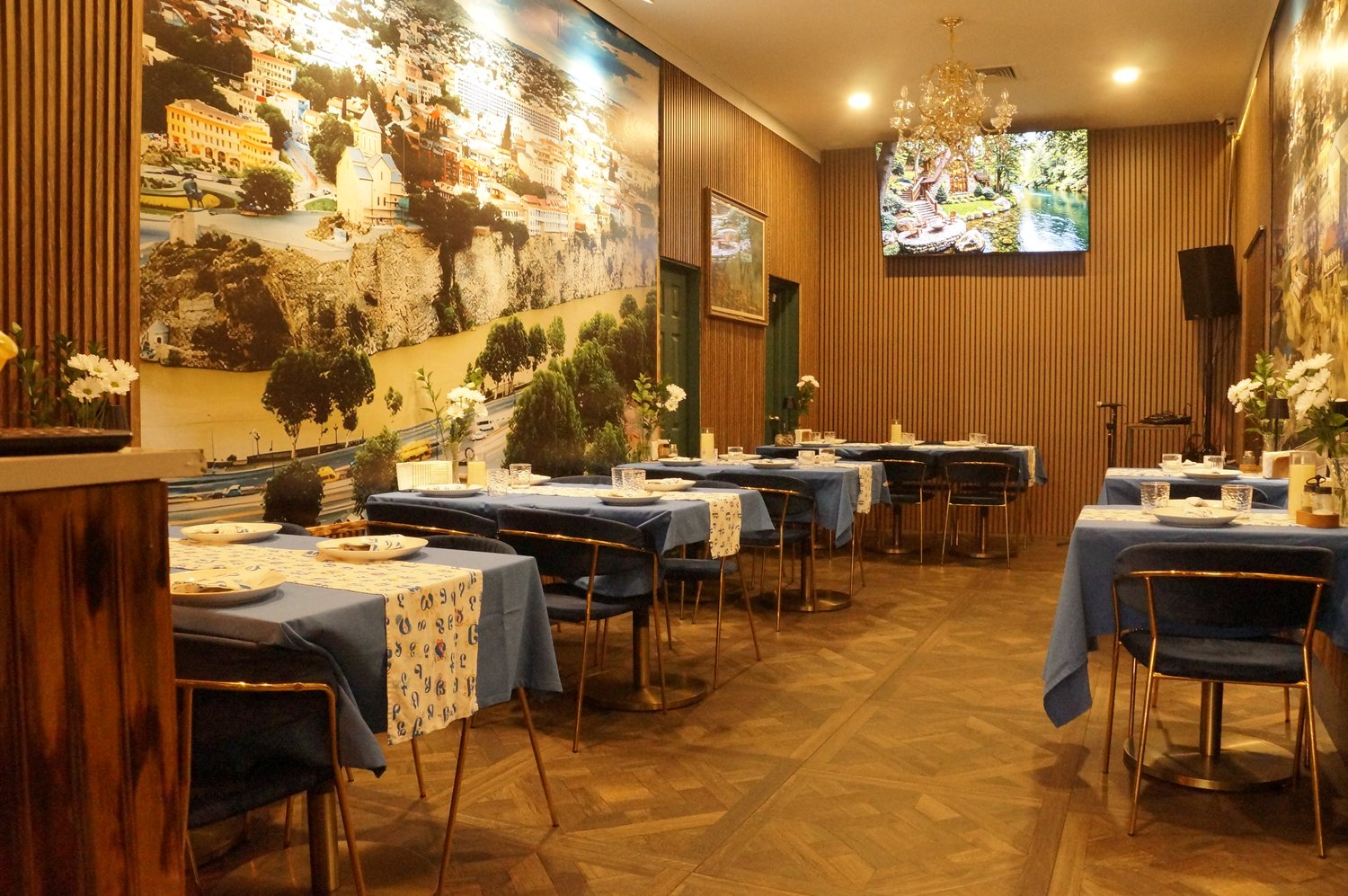 The dining room at Imereti — tables in blue linen with Georgian alphabet runners, wood-slat walls and a mural of old Tbilisi