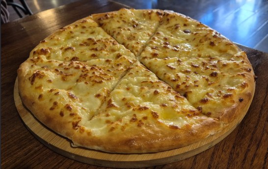Imeruli khachapuri — round Georgian cheese bread cut into wedges on a wooden board